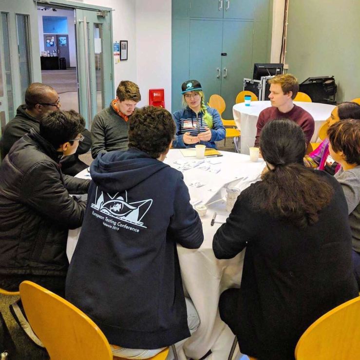 9 people sat around a round table that's covered in paper notes, and at the far side of the table, I am speaking while looking quite serious.